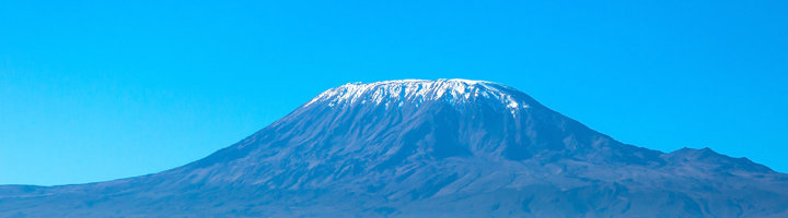 Besneeuwde top van de Kilimanjaro onder een heldere blauwe lucht.
