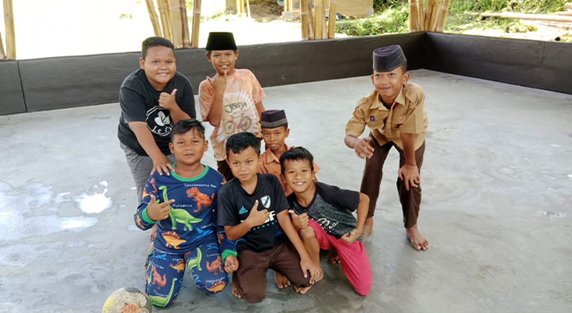 Groep jongens poseert lachend in een open paviljoen, enkele met traditionele petjes.