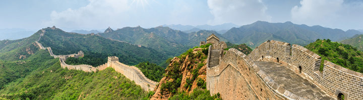 Panoramisch uitzicht op de Chinese Muur die over groene bergen slingert onder een blauwe lucht.