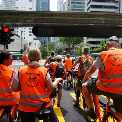 Groep fietsers met oranje veiligheidsvesten tijdens de fietstour Best of Kuala Lumpur in het stadscentrum.
