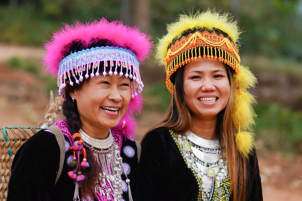 Twee lachende vrouwen in traditionele kleding met kleurrijke hoofdtooien tijdens 22-35ers reis Thailand, Laos & Cambodja.