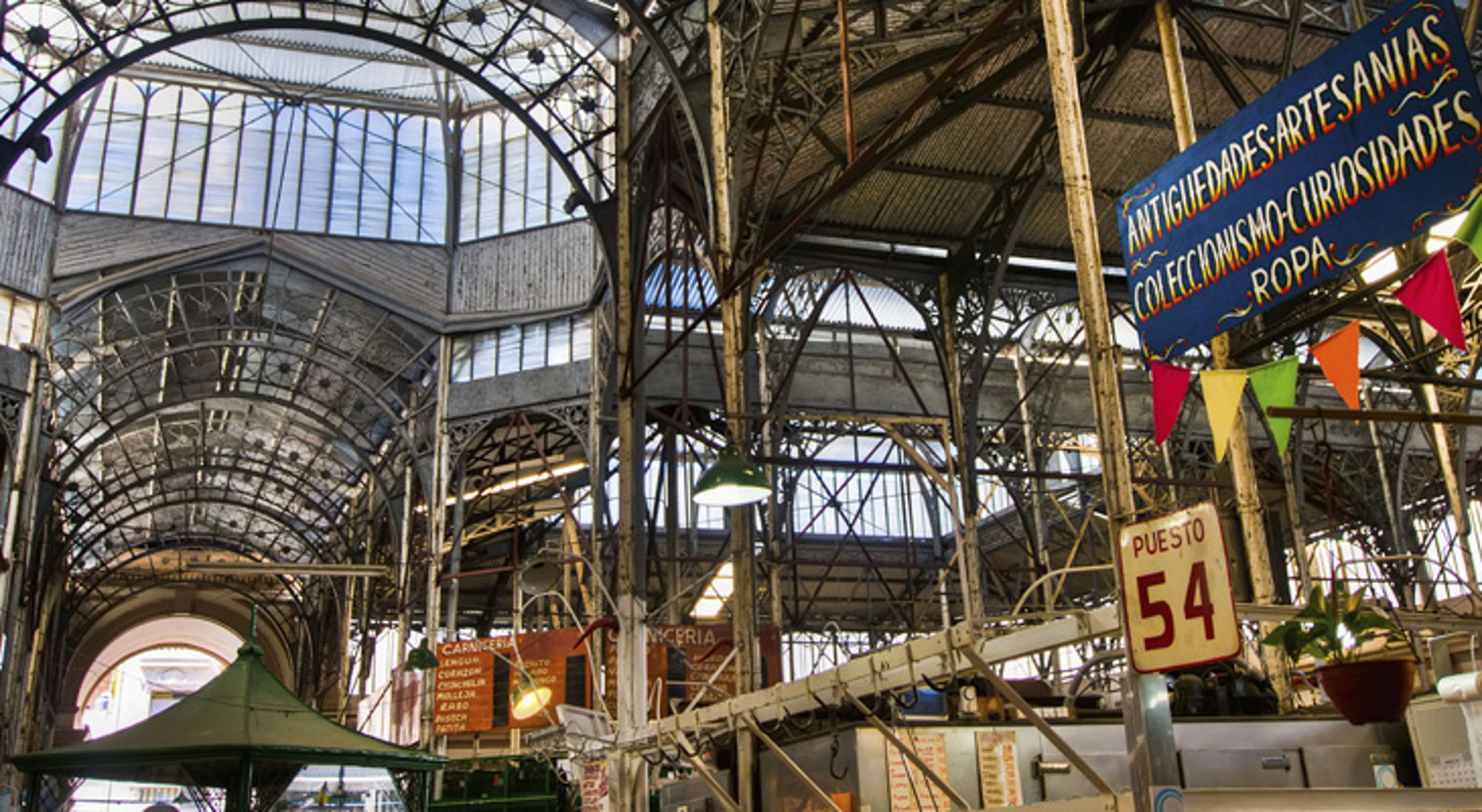 Lokale markten van Buenos Aires Overdekte markthal met gietijzeren bogen en kraampjes, met bordjes “Puesto 54” en “Antigüedades”.
