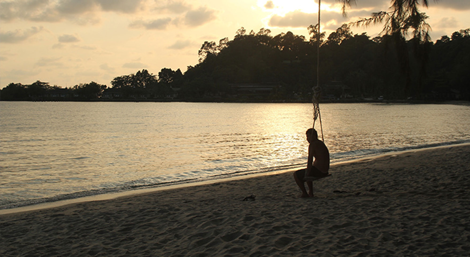 Olivier in Thailand Silhouet van een persoon op een schommel aan het strand bij zonsondergang.