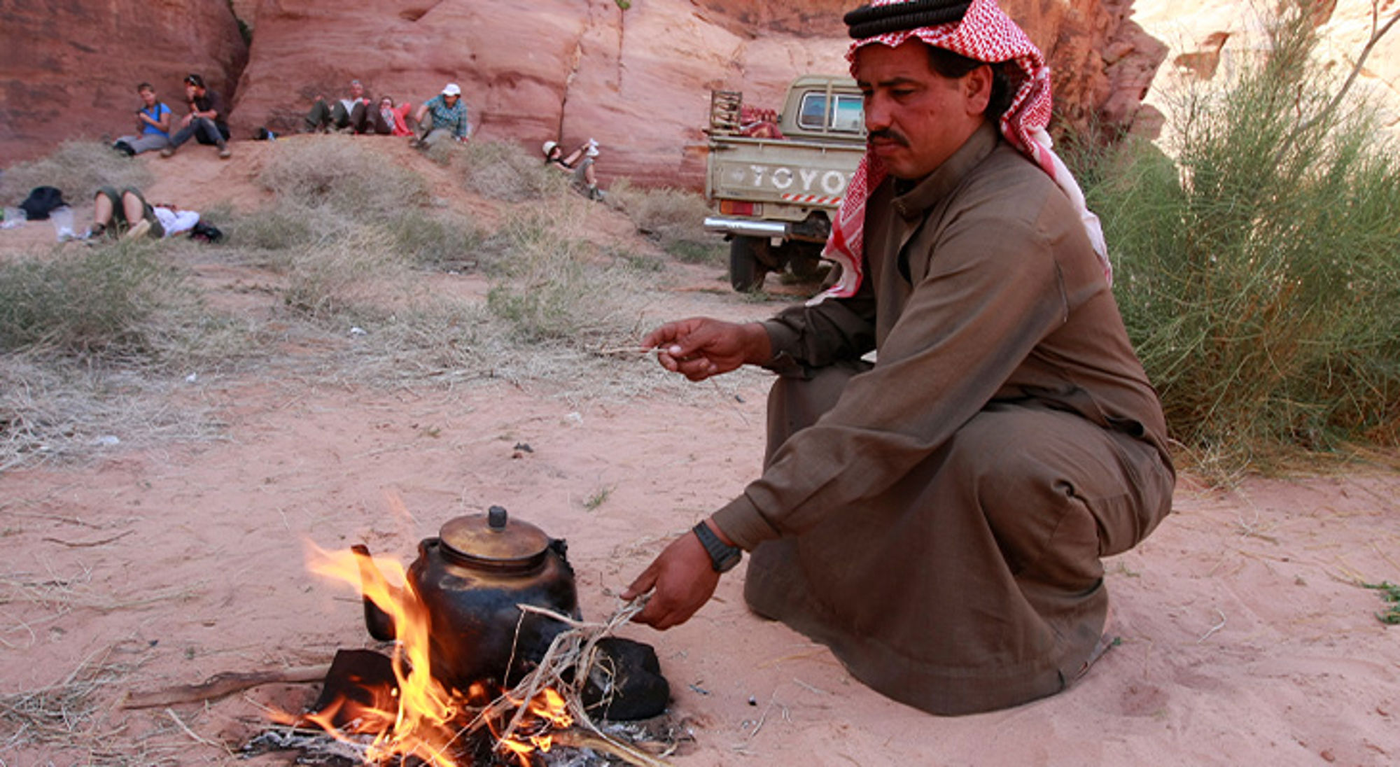 Bevolking Jordanië Man bereidt thee op een kampvuur in een rotsachtige woestijnomgeving.