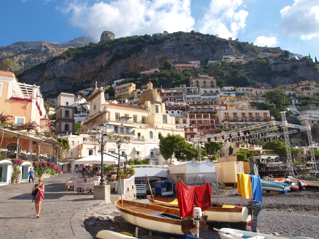 Kleurrijke huizen en kerkkoepel in Positano aan de Amalfikust, met boten op het strand.