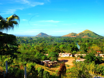 Groene heuvels en palmbomen in de Valle de Viñales, Cuba, met boerderijen onder een heldere blauwe lucht.