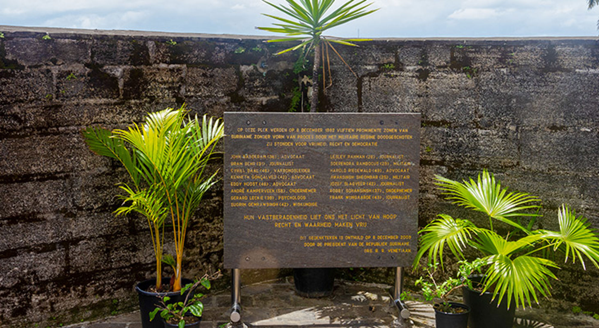 Gedenkplaat bij Fort Zeelandia in Paramaribo, omringd door palmen.