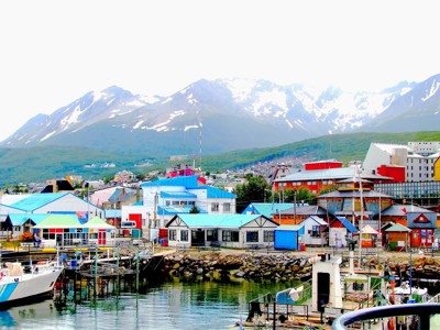 Ushuaia met kleurrijke havengebouwen en boten, met besneeuwde Andesbergen op de achtergrond.