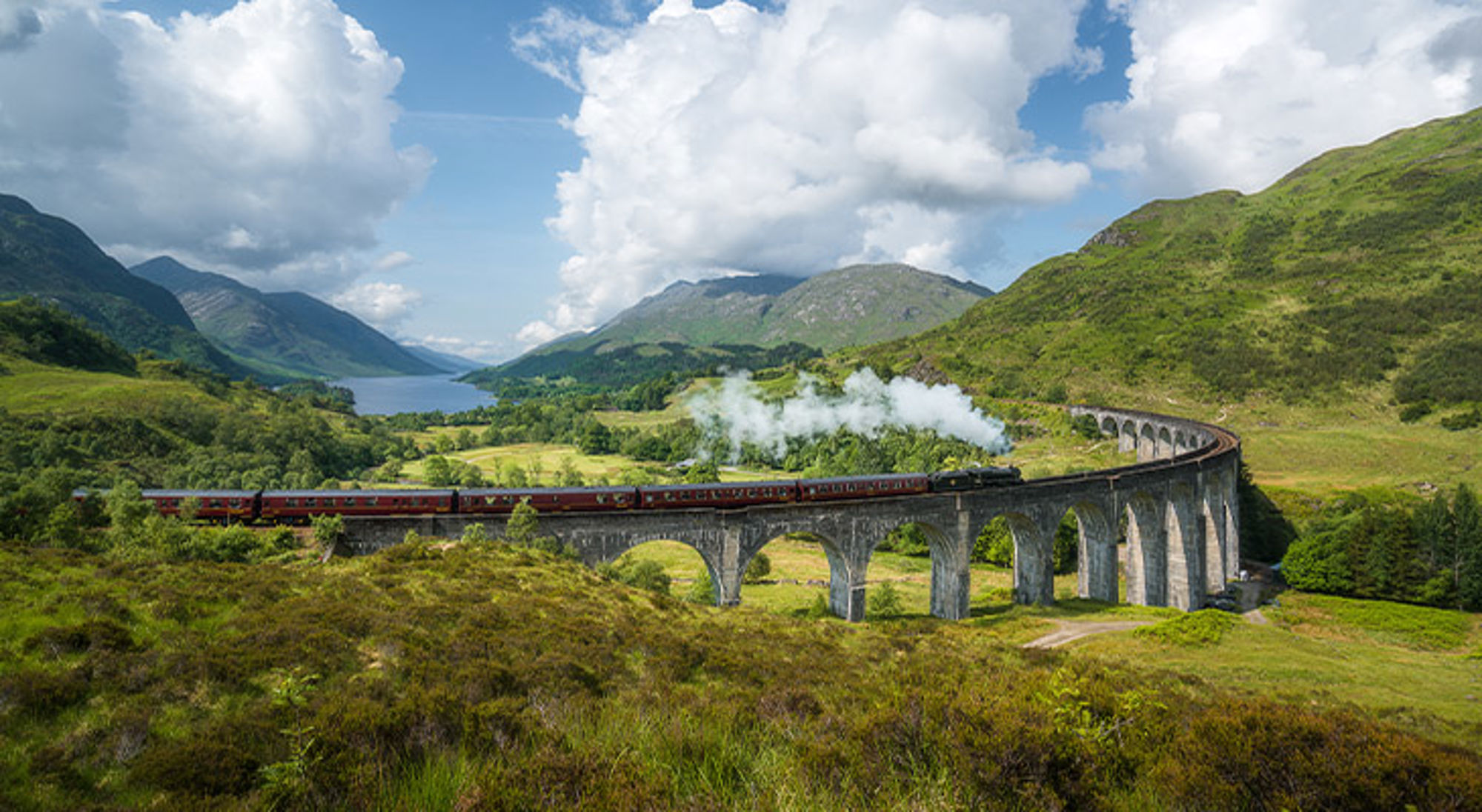 Jacobite stoomtrein op Glenfinnan viaduct Stoomtrein op het Glenfinnan-viaduct met bergen en loch op de achtergrond, Schotland.