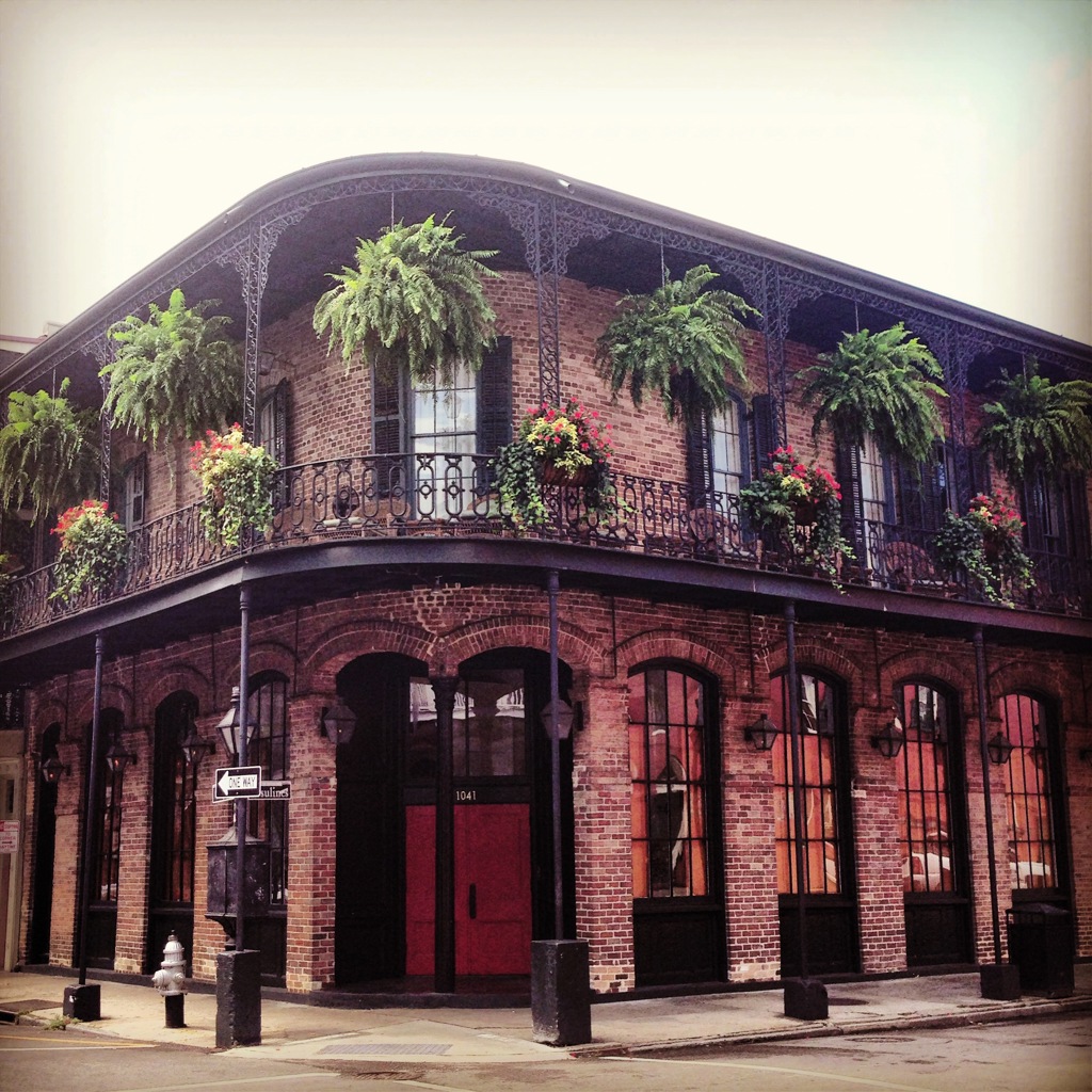 Historisch gebouw met gietijzeren balkon en hangende varens in de French Quarter, New Orleans.