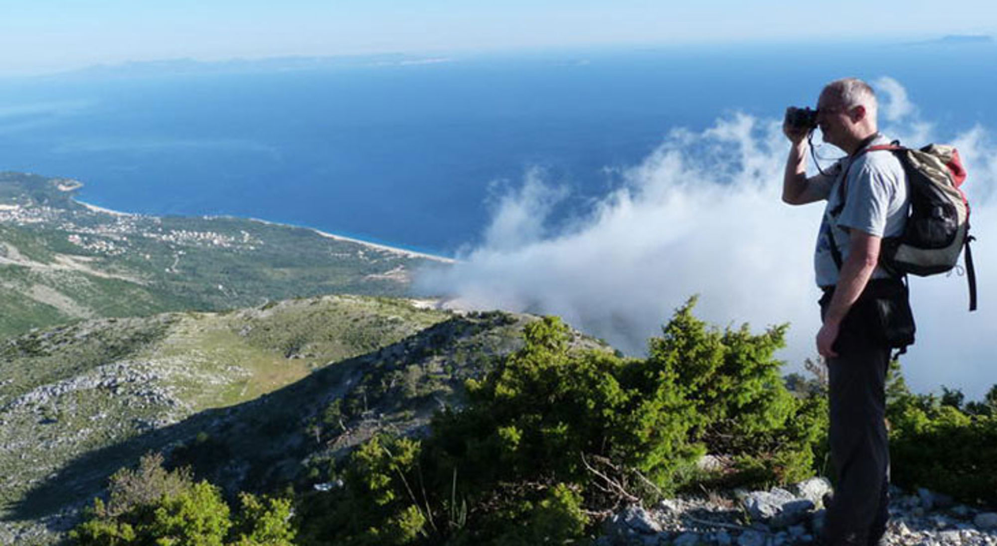 Single reis Albanië Wandelaar met rugzak maakt foto op bergtop met uitzicht op kustlijn en zee.