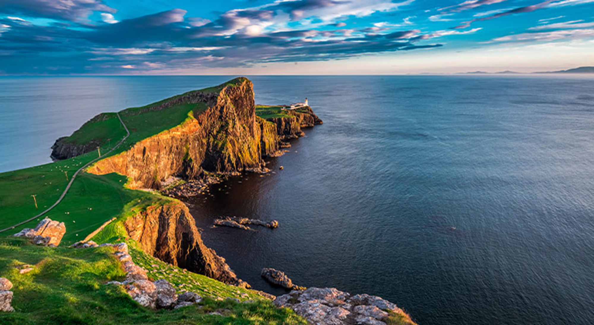Isle of Skye Groene kliffen met vuurtoren aan de kust van Isle of Skye, Schotland, bij zonsondergang.