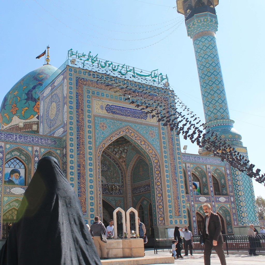 Blauwe mozaïekmoskee met koepel en minaret in Iran, met bezoekers op het plein.