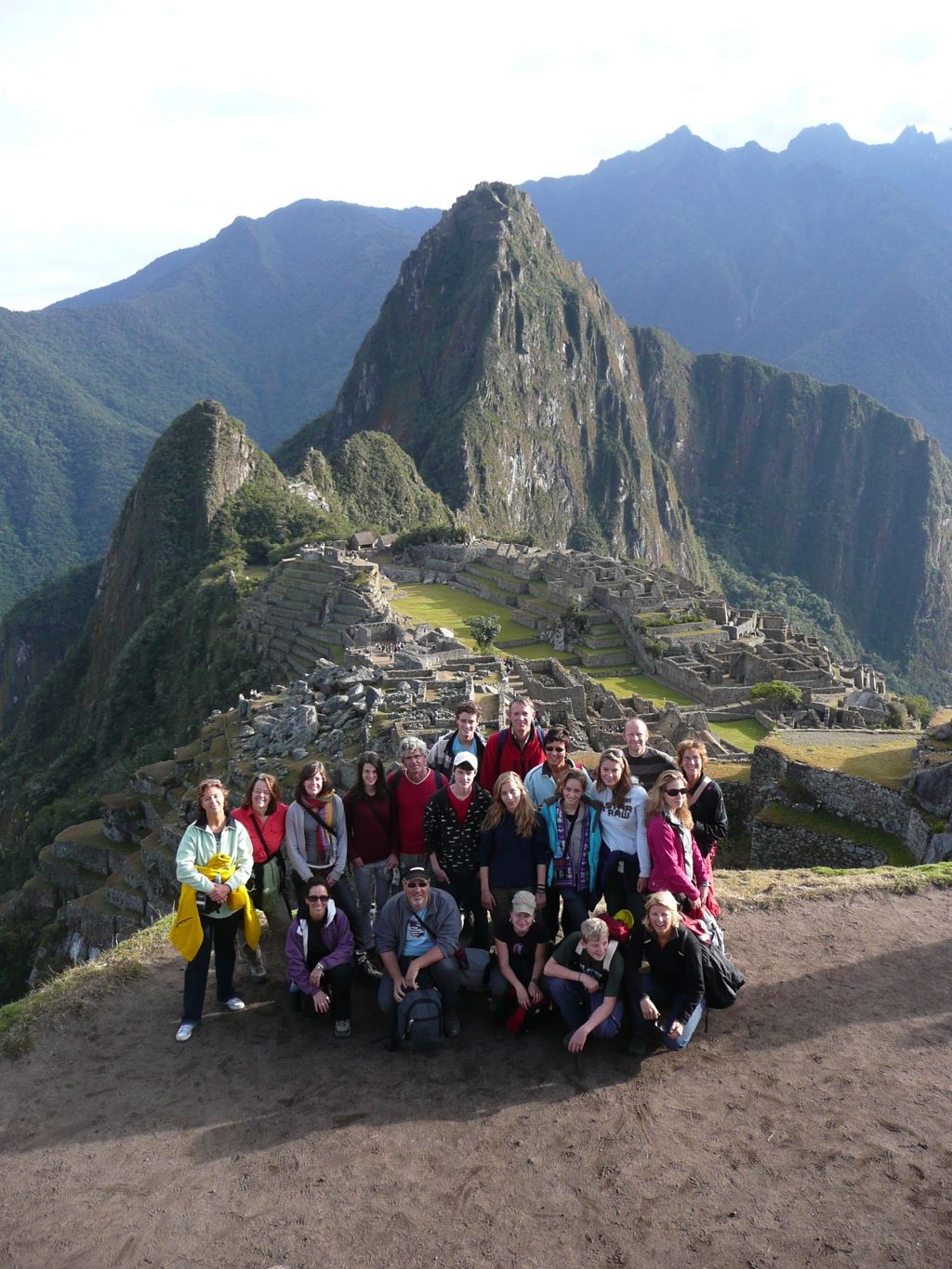 Groepsfoto van familiereis Peru bij Machu Picchu, met de Inca-ruïnes en Huayna Picchu op de achtergrond.
