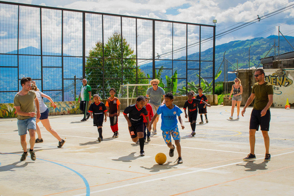 22-35ers spelen voetbal met lokale kinderen op een veld in Colombia, met bergen op de achtergrond.