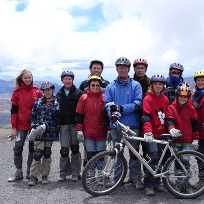 Gezin met mountainbikes en helmen op een hoogvlakte in Ecuador tijdens een familiereis, met bergen op de achtergrond.