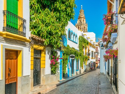 Kleurrijke straat in Córdoba met bloemen aan balkons en de toren van de Mezquita op de achtergrond.