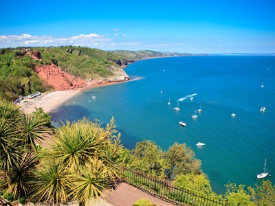 Uitzicht op de kust bij Torquay met rode kliffen, strand en zeilboten in de baai.