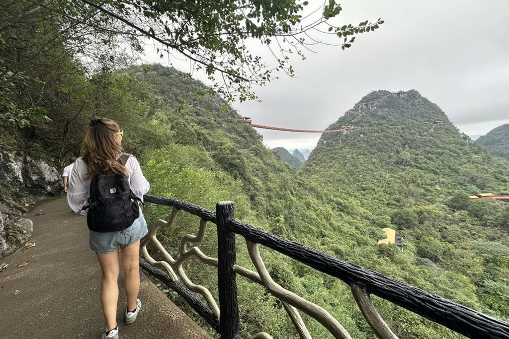 Wandelen over bergpad met uitzicht op een hangbrug tussen groene bergen tijdens groepsrondreis China.