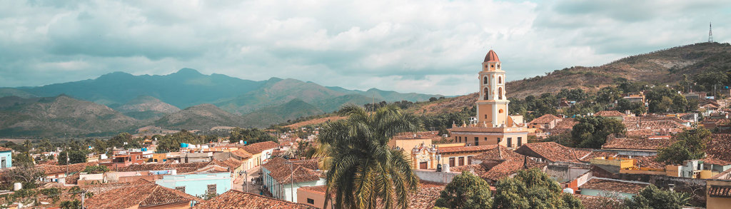 Panorama van Trinidad, Cuba met kleurrijke daken, palmbomen en kerktoren tegen de bergen.