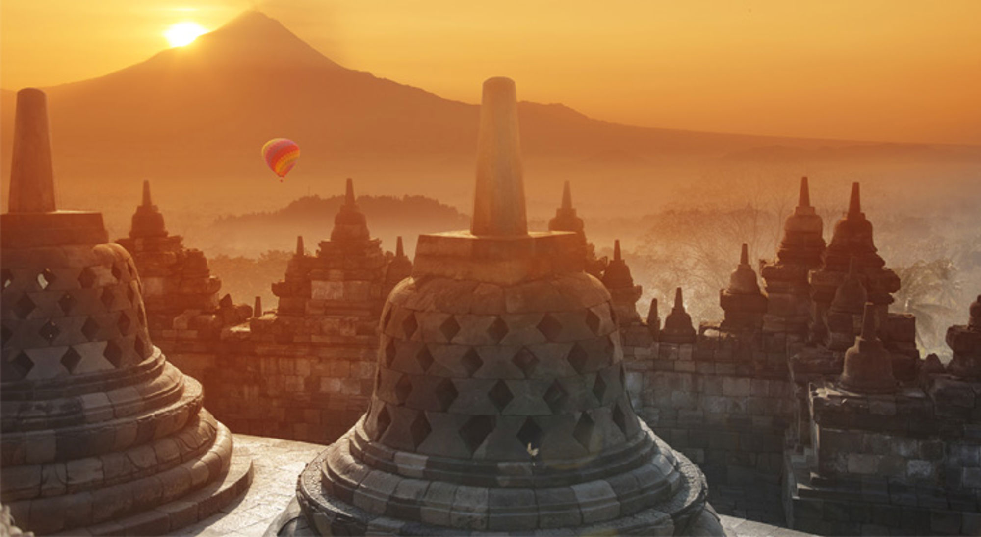 Zonsopkomst bij Borobudur-tempel op Java, met een luchtballon boven het mistige landschap.