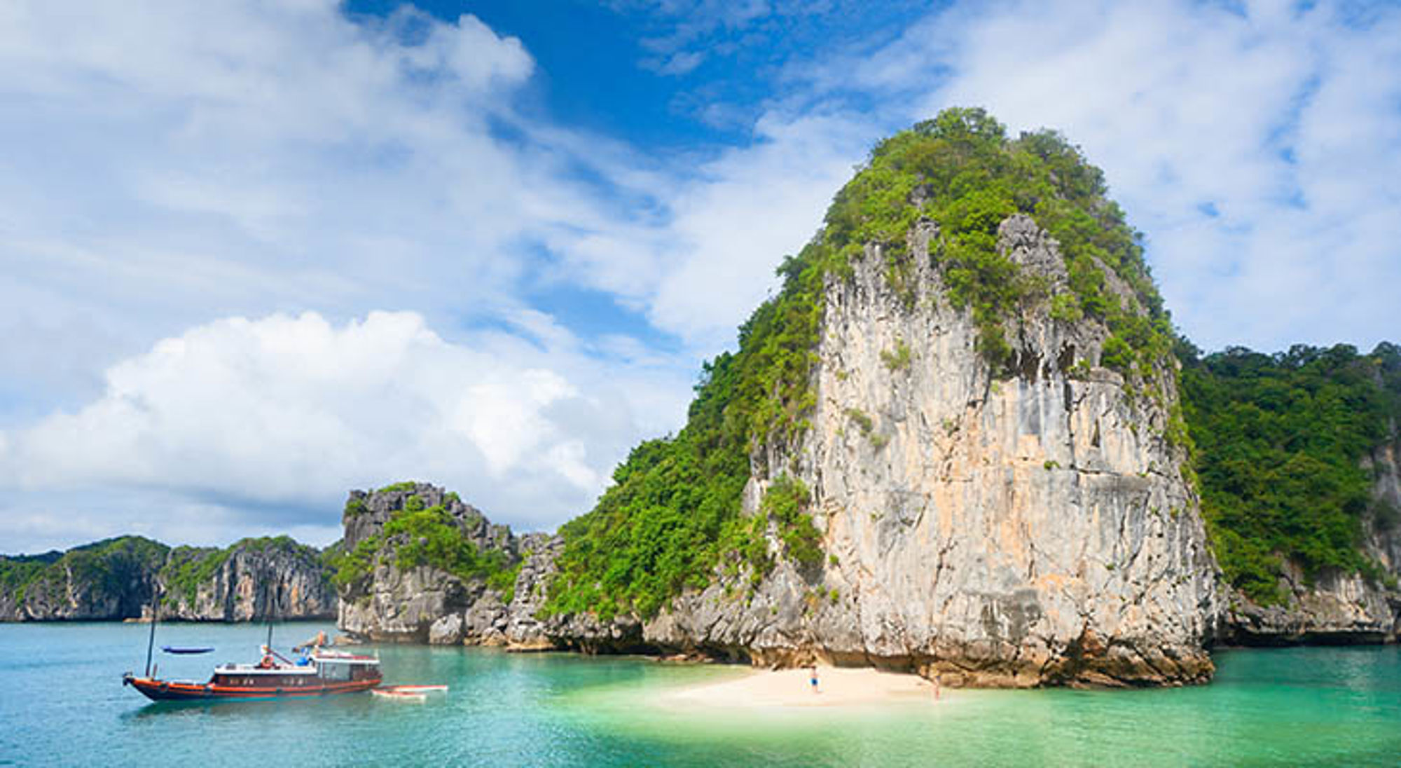 Cat Ba island Karstrotsen en strand in Halong Bay, Vietnam, met boot op helder turquoise water.