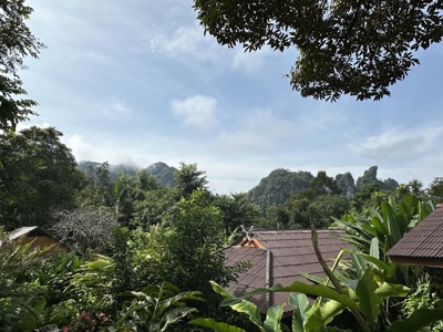 Groene jungle met bergtoppen en daken van bungalows in Thailand tijdens de route mei t/m september.