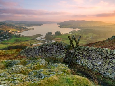 Uitzicht over Lake Windermere in het Lake District bij zonsondergang, met stenen muurtje en houten trap.