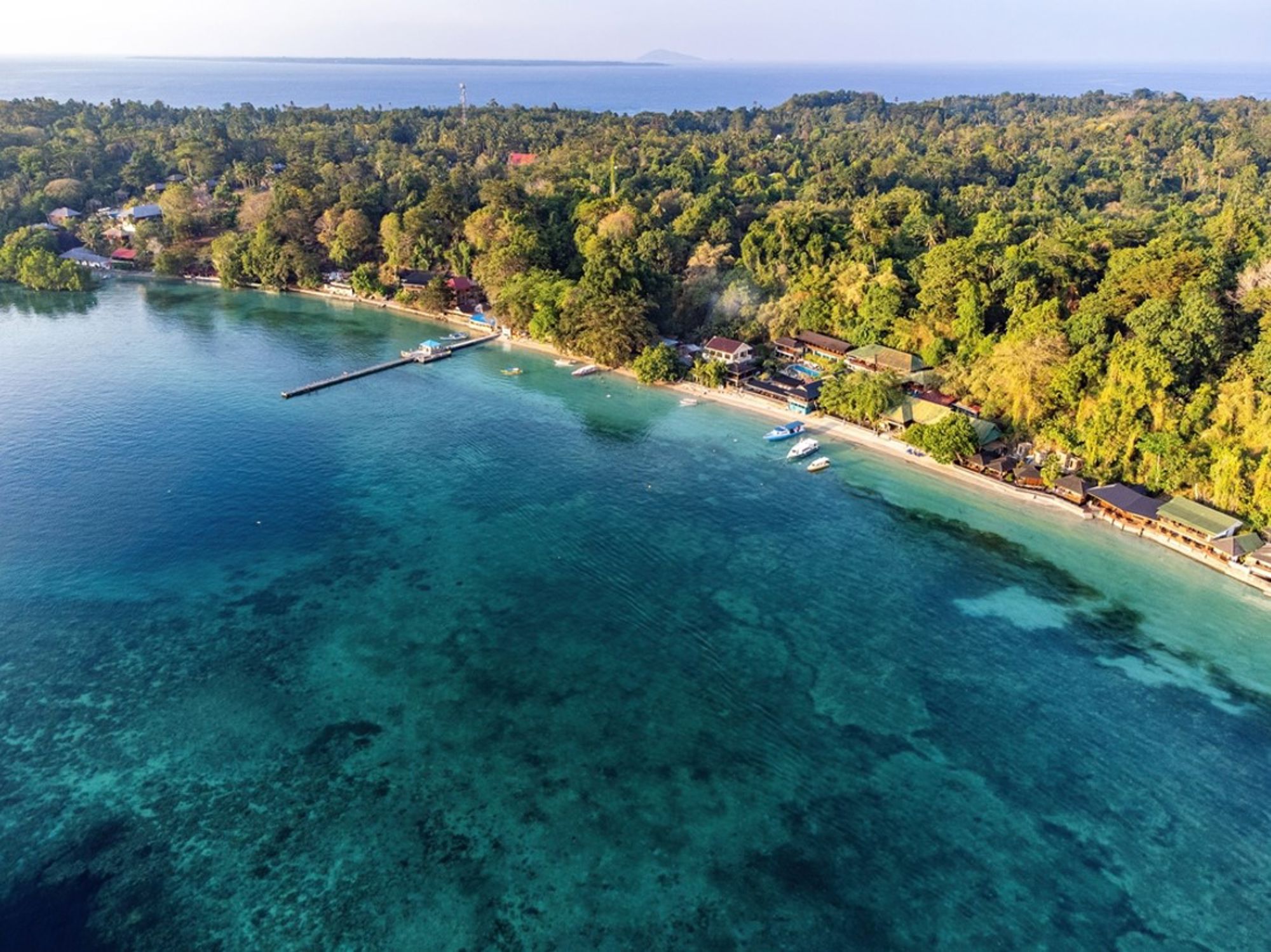 een tropische kustlijn in Indonesië met helderblauw water, strand en beboste heuvels.
