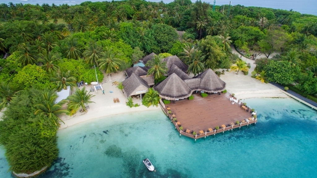 Overwaterresort met rieten daken aan wit zandstrand en turquoise lagune op de Malediven.