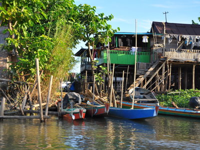 Houten paalwoningen aan de rivier met kleurrijke bootjes in Kalimantan tijdens de rondreis Kalimantan, Sulawesi & Molukken.