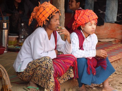 Twee vrouwen met traditionele hoofddoeken zitten bij een huis in Myanmar tijdens de route van 17 dagen.