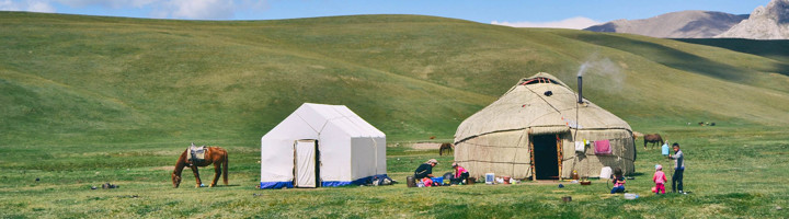 Nomadentent en yurt op groene steppe langs de Zijderoute, met grazend paard en bergen op de achtergrond.