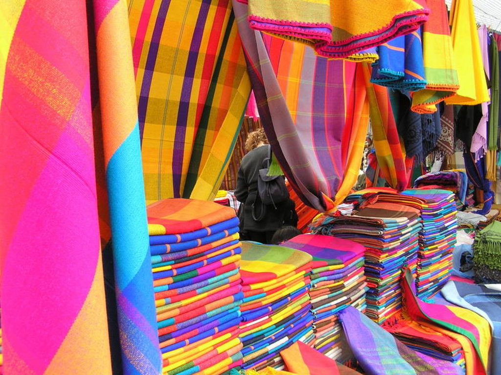 Kleurrijke stapels geweven dekens en doeken op een markt in Ecuador tijdens een familiereis.