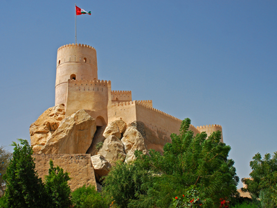 Fort met ronde toren en Omaanse vlag op rotsen, route Oman en Dubai.