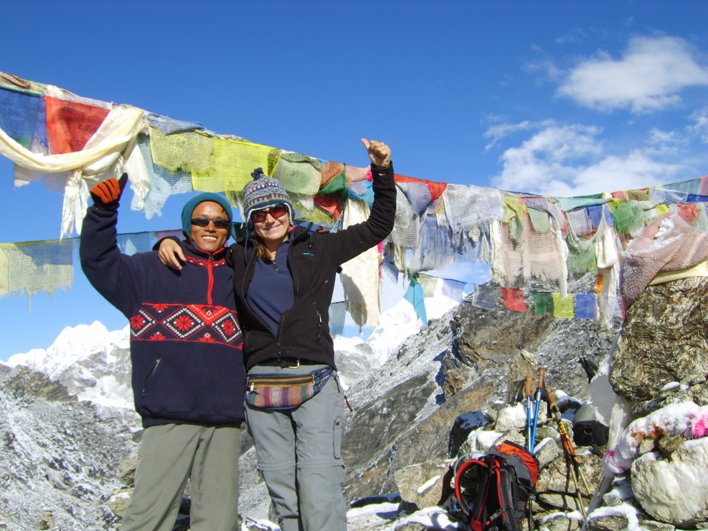 Twee wandelaars bij gebedsvlaggen tijdens de Everest-trektocht in Nepal, met besneeuwde bergtoppen op de achtergrond.