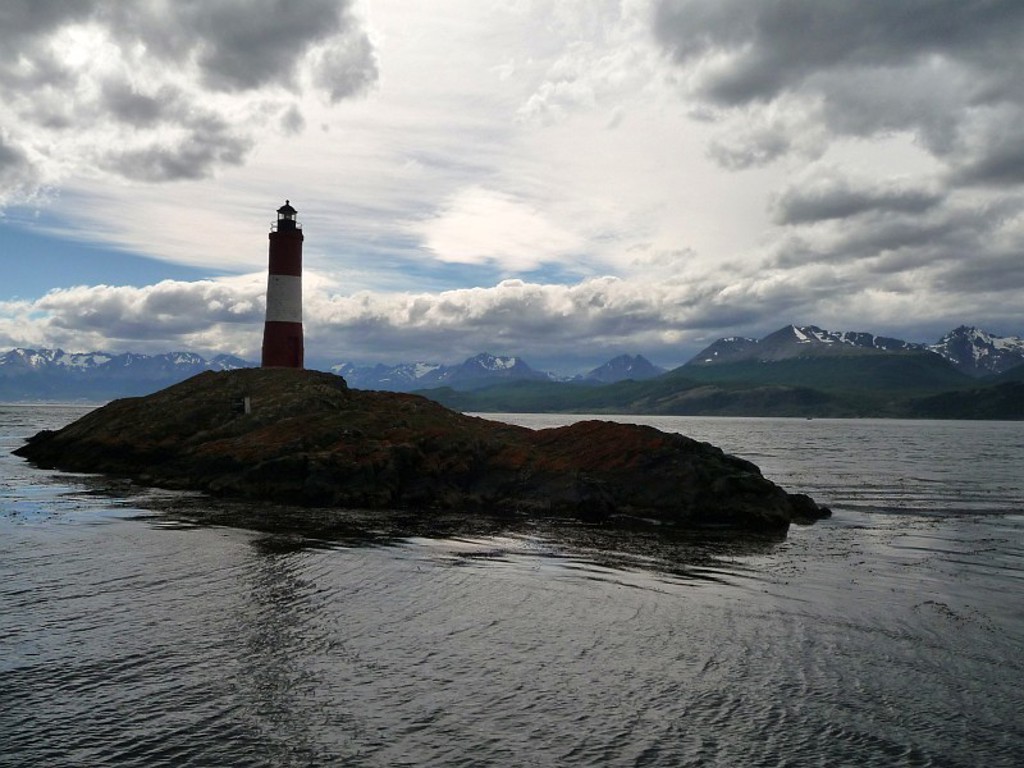 Vuurtoren op rotsachtig eilandje met bergen op de achtergrond tijdens een groepsrondreis door Argentinië.