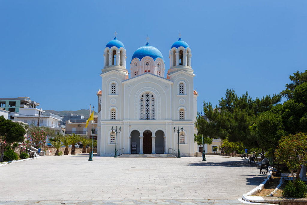 Wit-Griekse kerk met blauwe koepels op Evia, Griekenland, onder een heldere blauwe lucht.