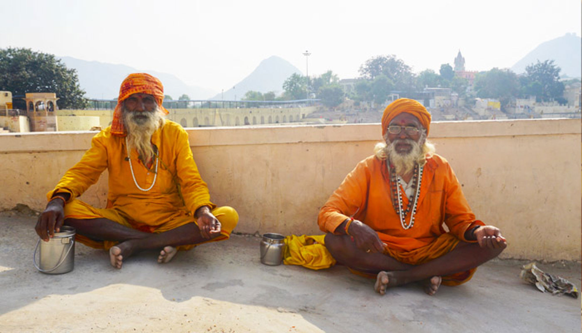 Lokale bevolking in India Twee mannen in oranje gewaden zitten in kleermakerszit op een terras met bergen op de achtergrond.