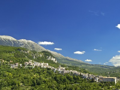 Panorama van een bergdorp in de Centrale Apennijnen met groene hellingen en hoge bergen onder een blauwe lucht.