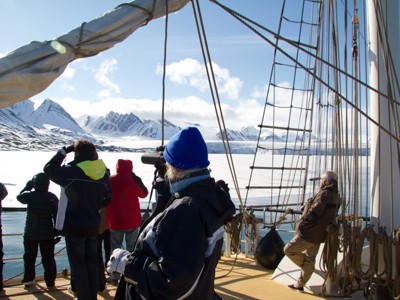 Passagiers op dek van zeilschip Antigua bekijken met verrekijker besneeuwde bergen en zee-ijs bij Spitsbergen.