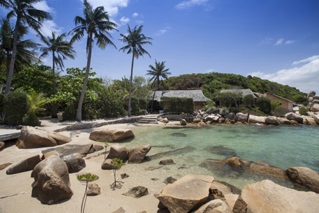 Tropisch strand in Vietnam met palmbomen, rotsen en helderblauw water.