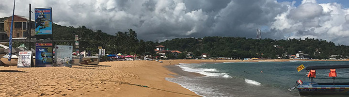 Zandstrand aan de kust van Sri Lanka met een boot op het water en donkere wolken boven de baai.