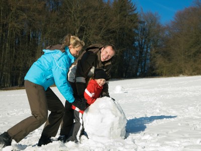 Gezin rolt een grote sneeuwbal in een besneeuwd landschap tijdens Route Lapland winter familiereis.
