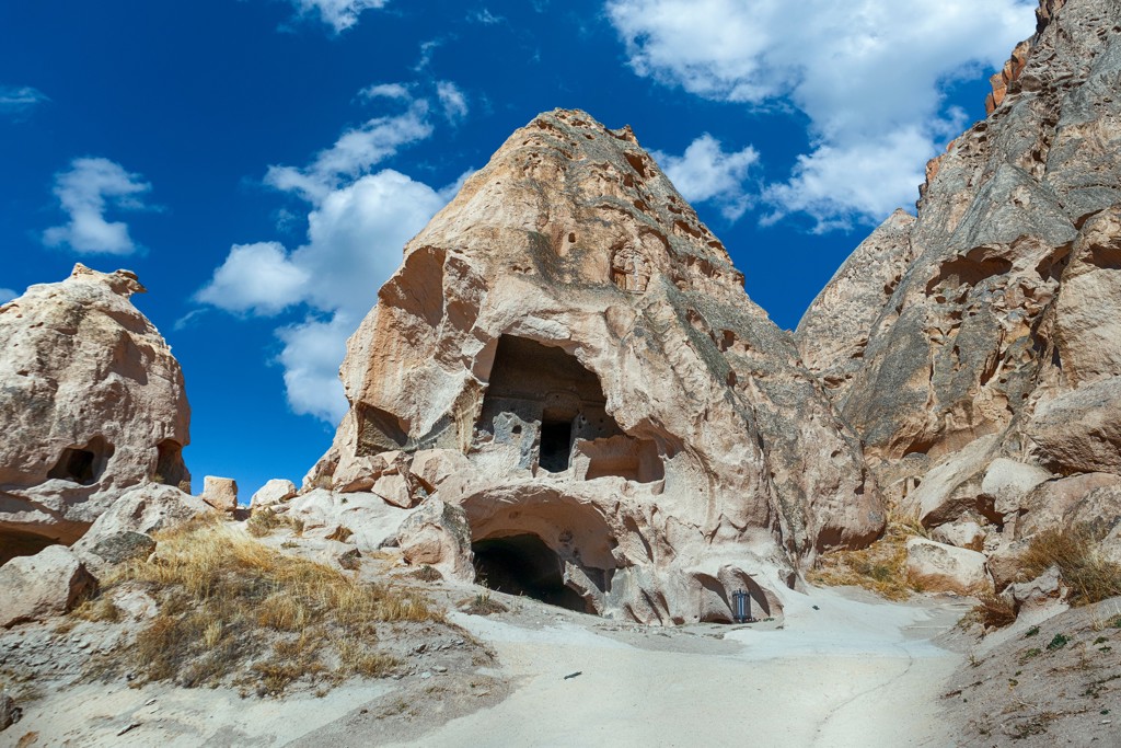 Rotsformaties met uitgehakte grotwoningen in Cappadocië, Turkije, langs een wandelpad onder blauwe lucht.