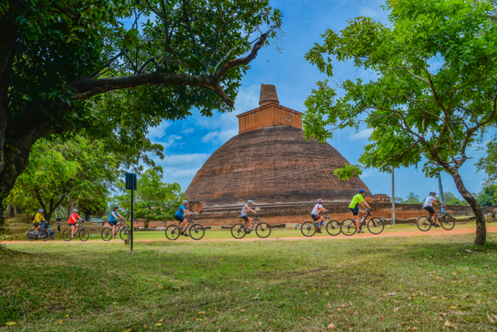 Fietsers tijdens een fietsvakantie in Sri Lanka langs een grote stoepa tussen groene bomen.