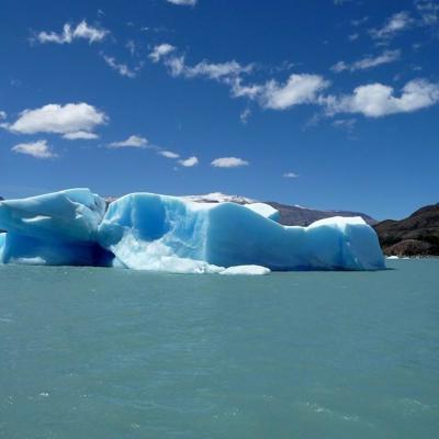 Blauwe ijsberg drijvend in een azuurblauw meer in Patagonië, met bergen op de achtergrond.
