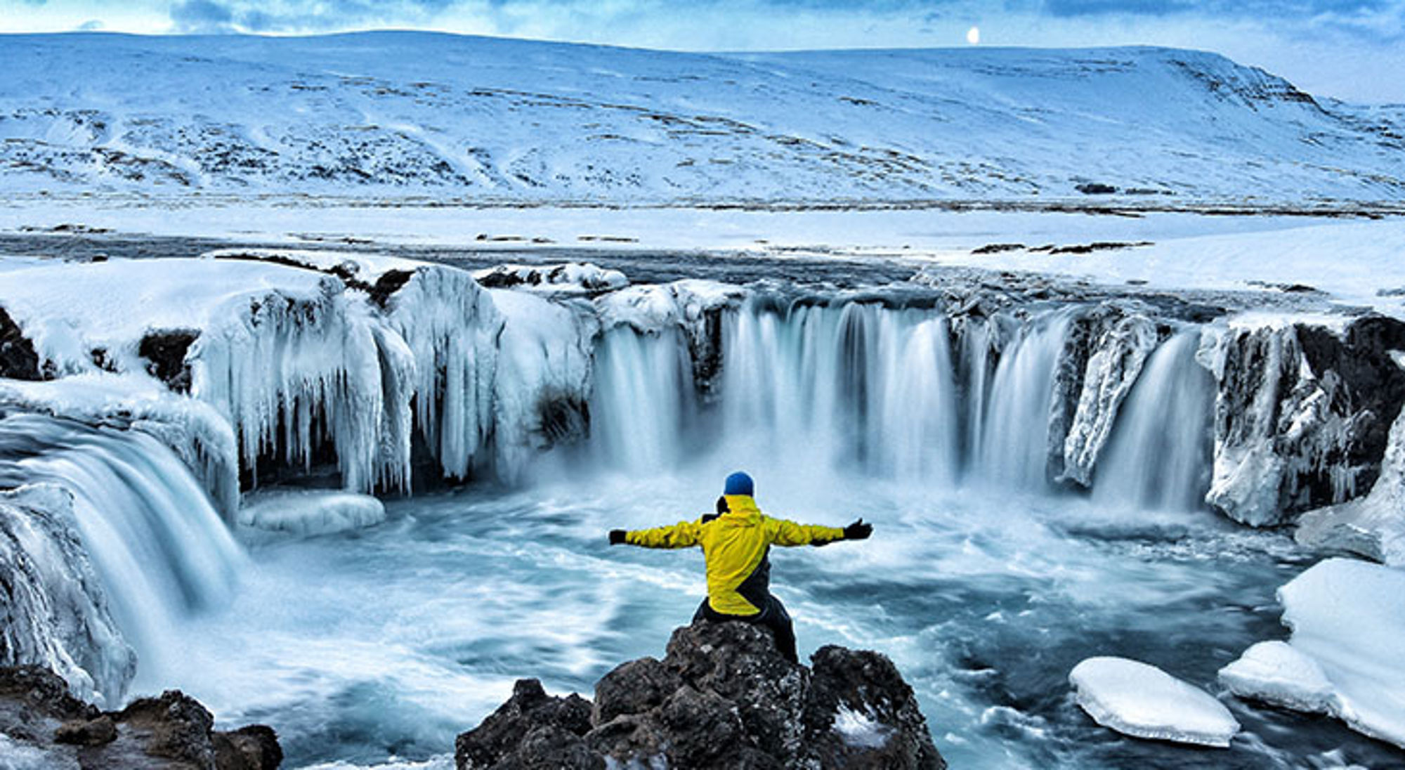Single reis IJsland Reiziger in gele jas bij bevroren waterval in winters landschap.