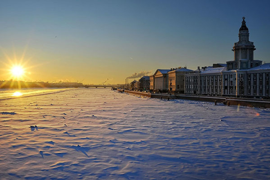 Zonsondergang boven een bevroren rivier met historische gebouwen langs de kade tijdens een groepsrondreis Rusland winter.