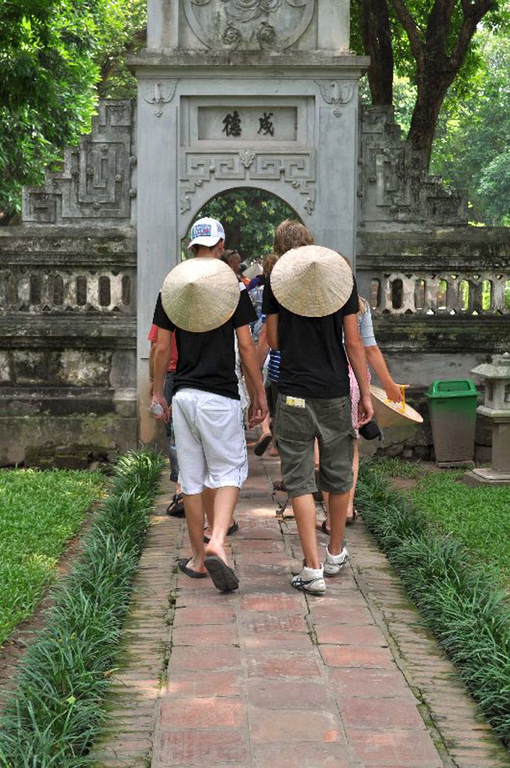 Reizigers met Vietnamese hoeden lopen door een tempelpoort tijdens groepsrondreis Vietnam kort.